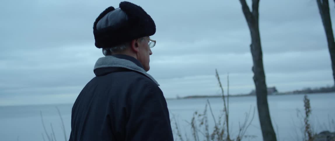 Man wearing a winter hat and coat walks along a lake