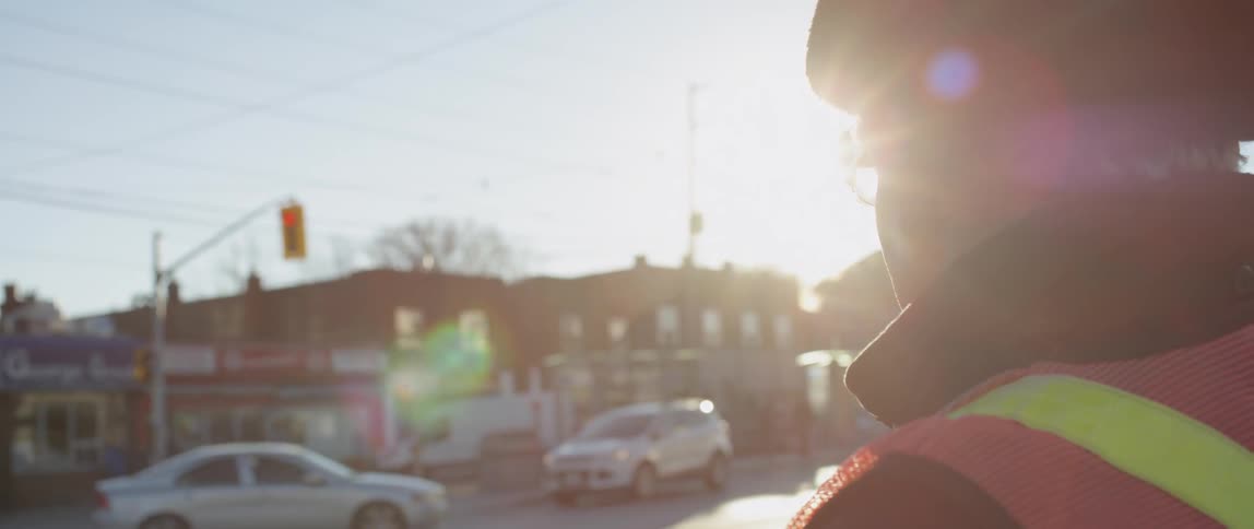 Elderly man stands on a busy intersection shielding his eyes from the sun