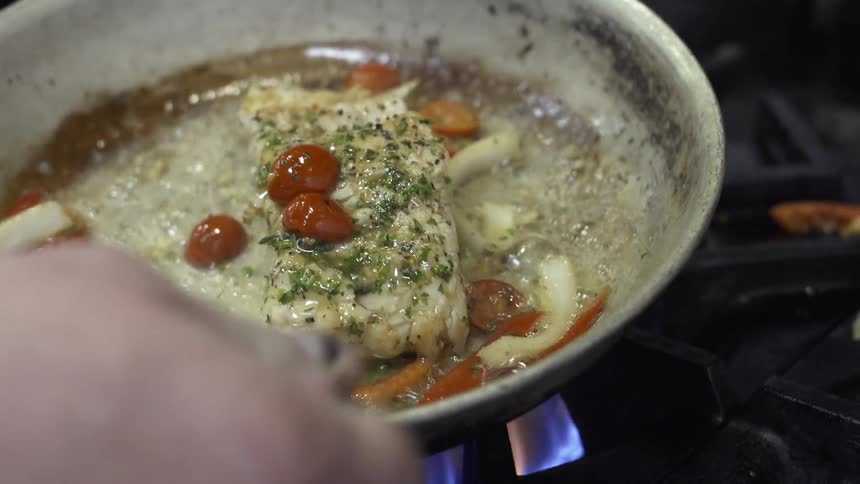 Person is cooking and basting fish in pan over stove