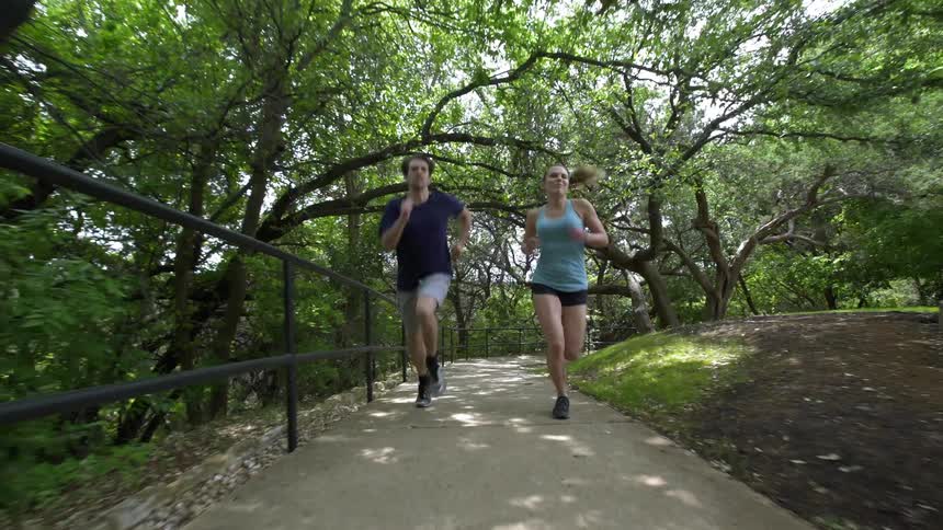Man and woman are jogging on footpath in shady park