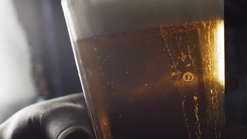 A hand holds a foamy glass of beer