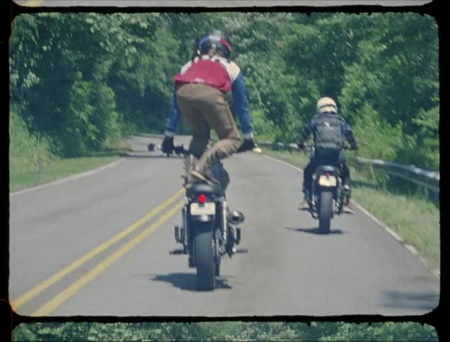 Man rides a motorcycle while standing on the seat