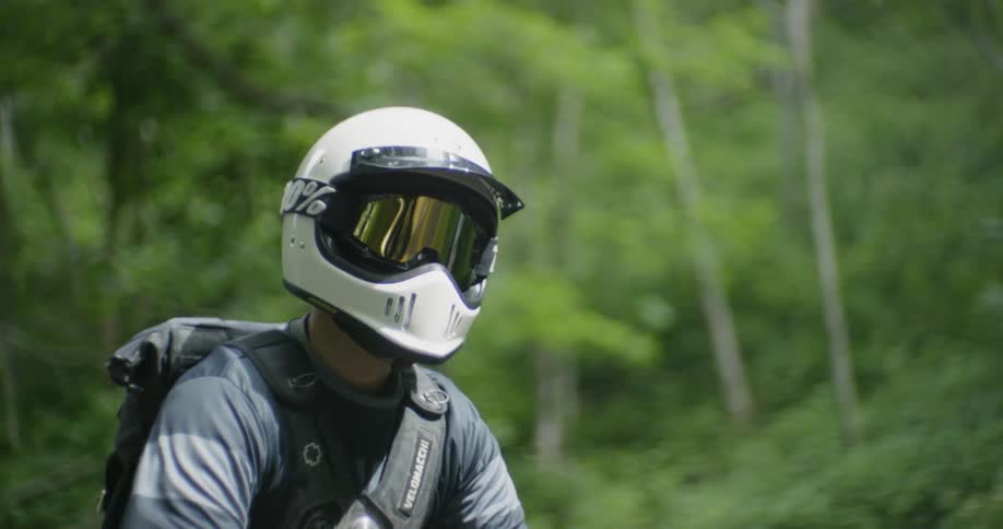 Man in a white helmet rides a motorcycle near the trees