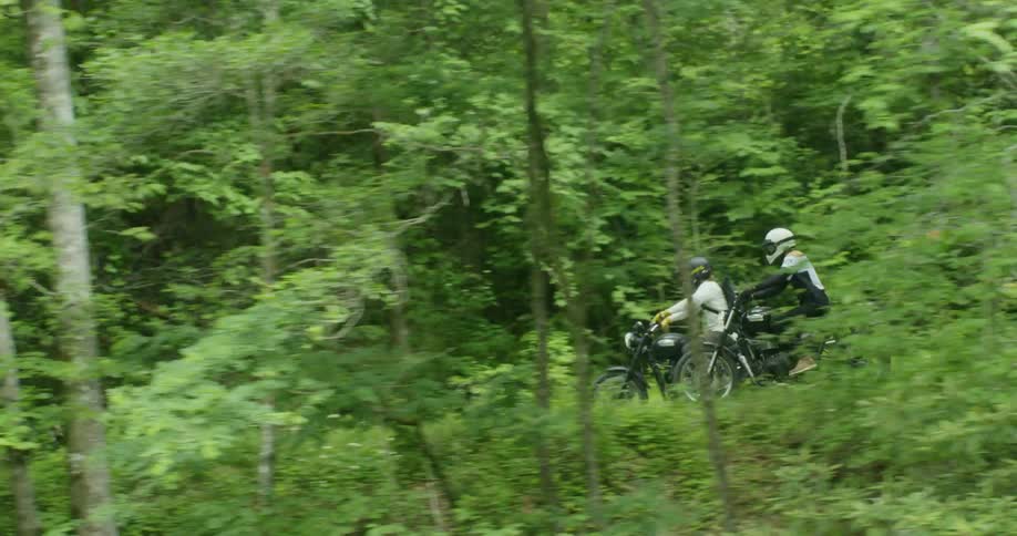Two people ride motorcycles on a trail in the woods