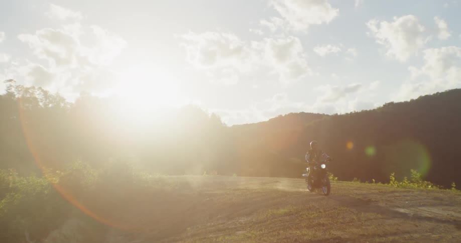 A person rides a motorcycle on a dirt road on a sunny day