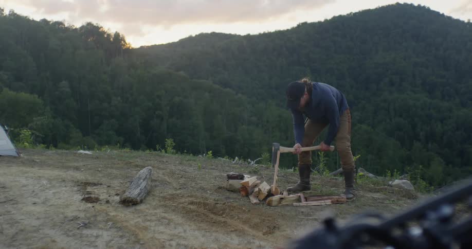 Man is splitting firewood with axe in the wilderness