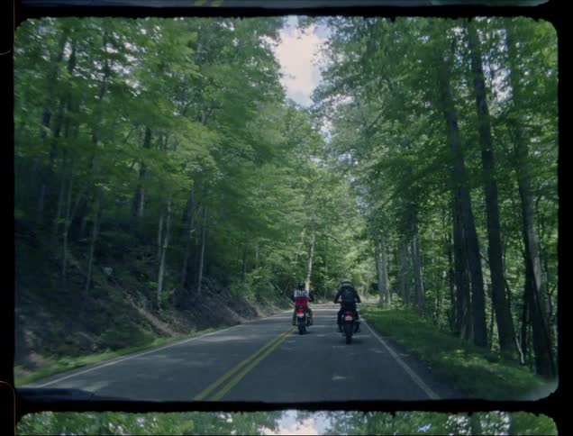 Two people are riding motorcycles on shady forest highway