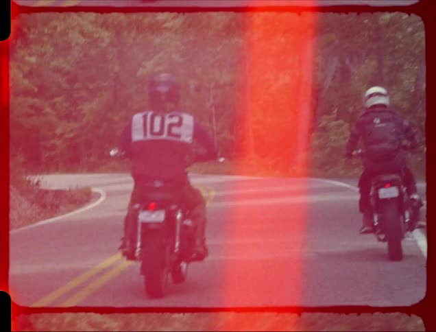 Two motorcycles travel around the bend in a highway