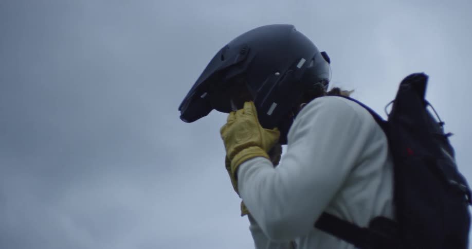 Man wearing helmet and backpack is standing outside on cloudy day