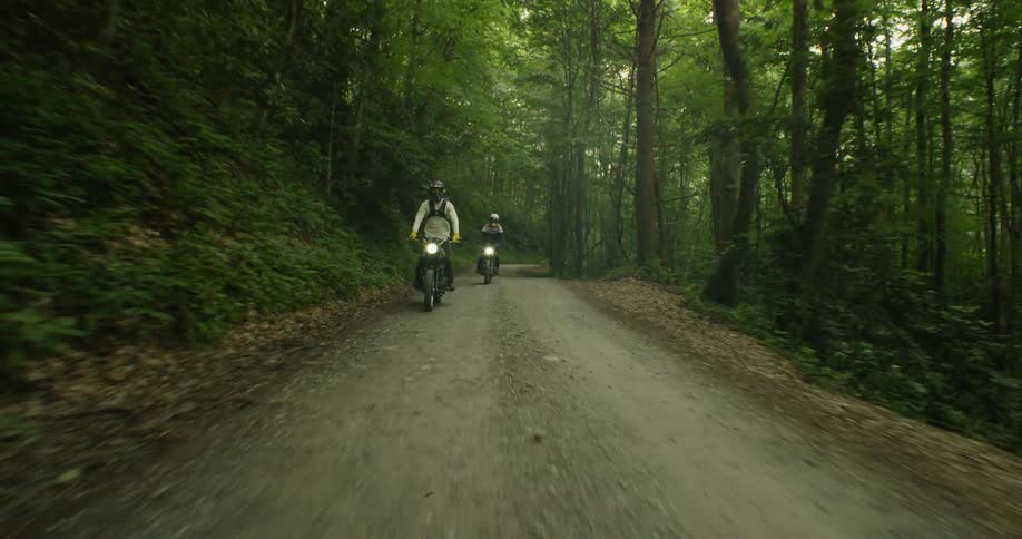 Two people are riding motorcycles on dirt road in forest area