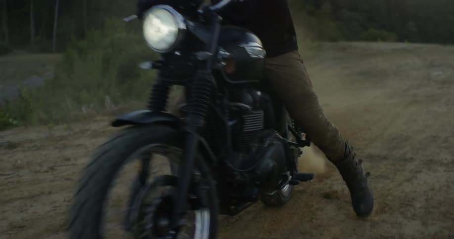 A man takes off on a motorcycle on a dirt road