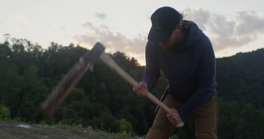 Man is splitting firewood with axe at campsite