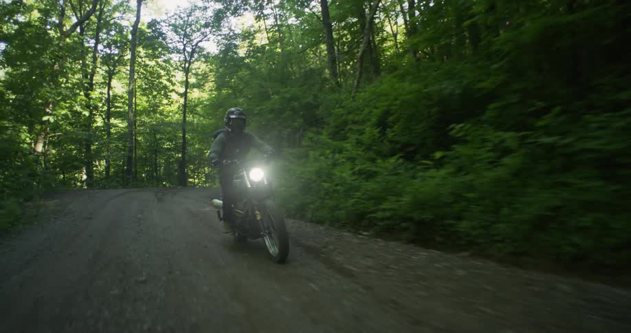 Person riding motorcycle on dirt road in forest area