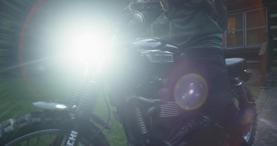 A man gets on a motorcycle turns on the headlight and rides away