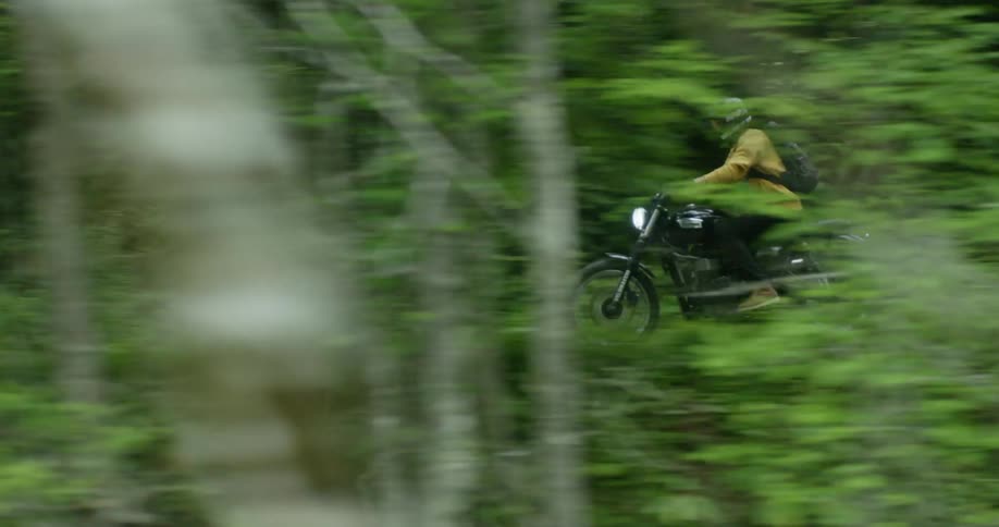 A person rides a motorcycle on a trail through a forest