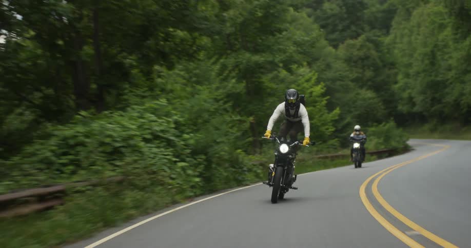 Two men ride motorcycles on a winding road