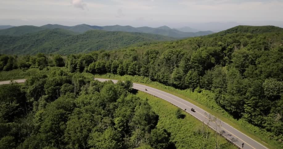 Two motorcycles travel on a mountain road on a sunny day