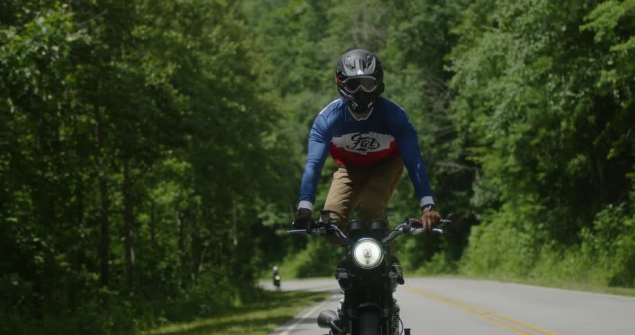 A motorcyclist stands on their bike on a rural road