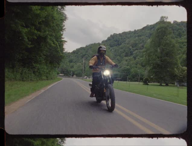 Man rides a motorcycle down the road near the trees
