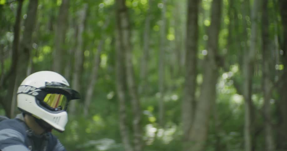A man rides a motorcycle on a woodsy road