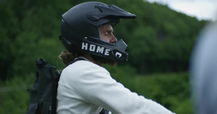A man wearing a helmet and backpack turns his head and smiles