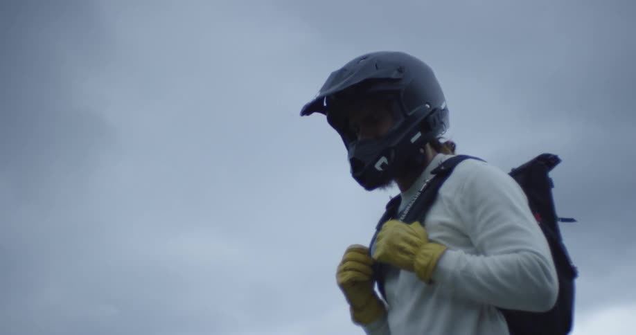 Two men wearing motorcycle helmets are outside on cloudy evening