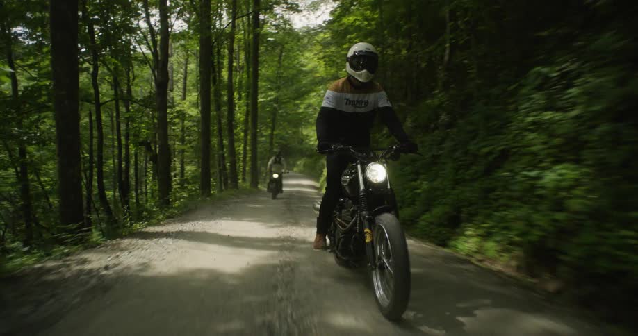 Two people are riding motorcycles on dirt forest road