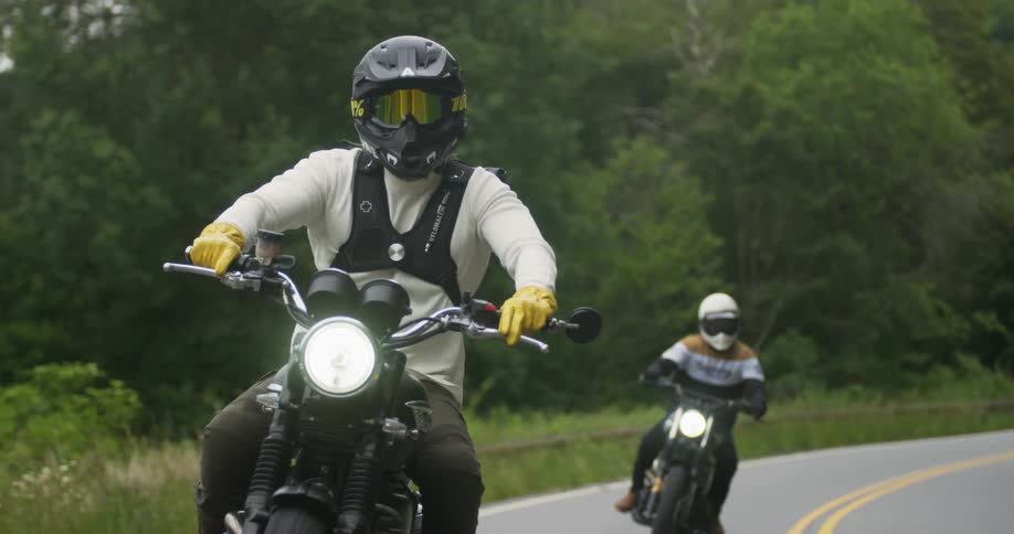 Two people ride motorcycles on a rural road