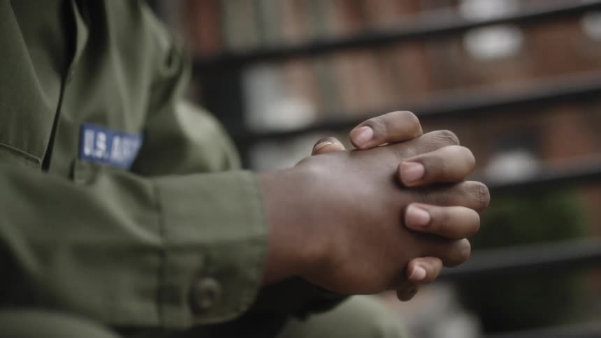 A service member sits with their hands clasped