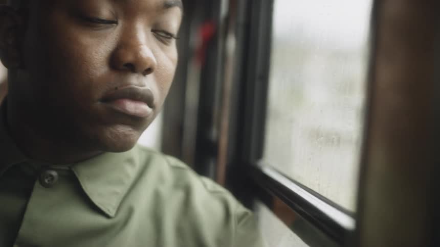 Man removes his hat as he sits in a train