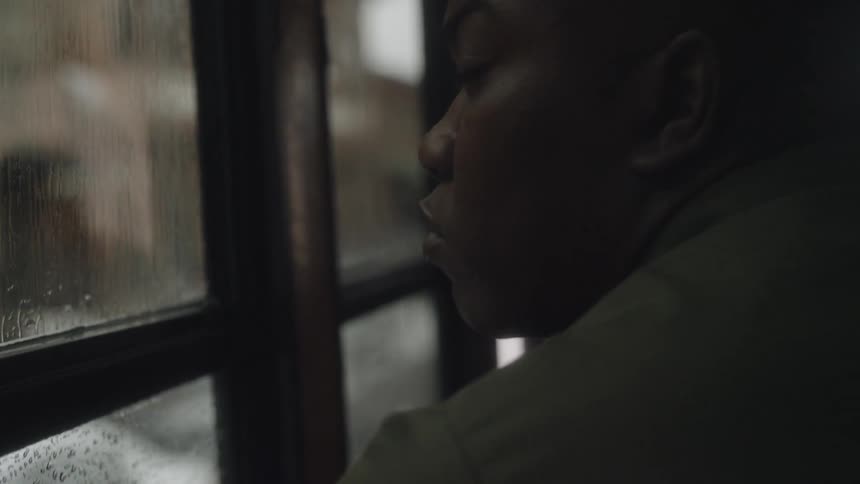 A man looks out a bus window while it rains