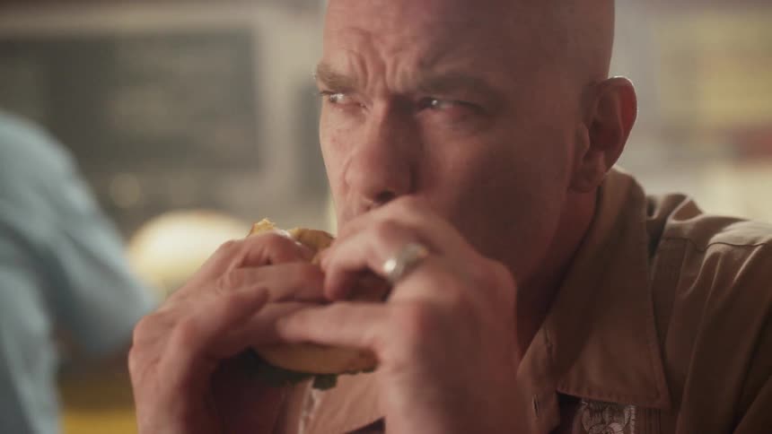 A man bites into and eats a burger at a table in a diner