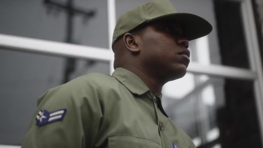 An airman stands in front of a building and looks up