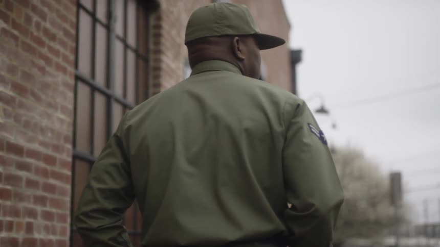 Man wearing a cap walks near a red brick building