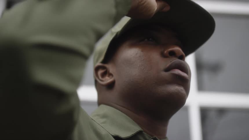 Man adjusts his cap as he stands near a building