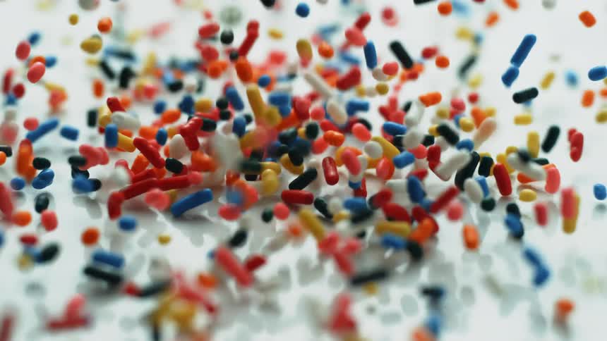 Colorful sprinkles fall onto a white surface