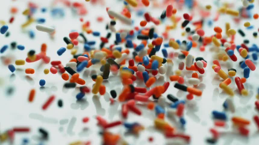 Colorful sprinkles fall onto a white surface