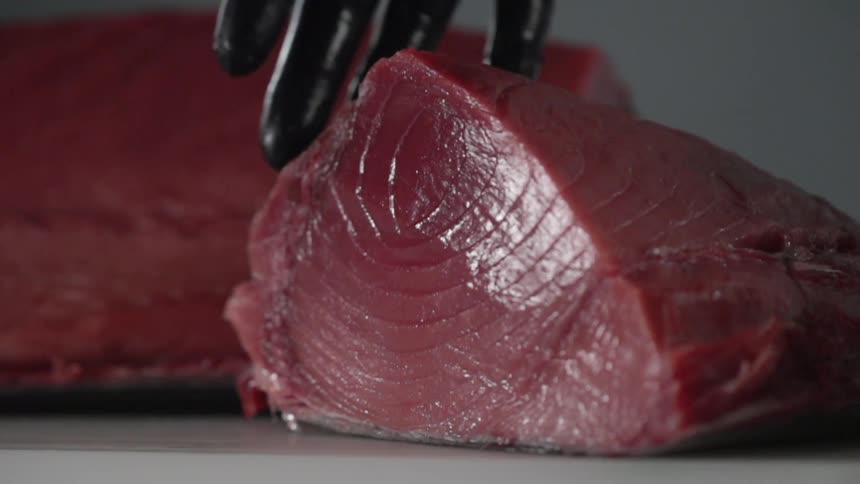 A person drops a large piece of fresh tuna