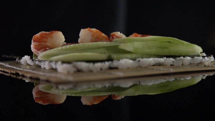 A person adds cucumber slices on top of shrimp seaweed and rice