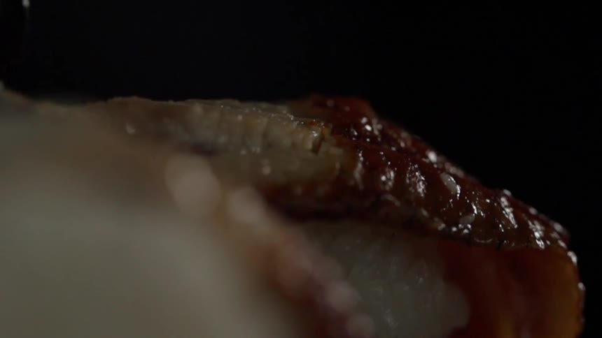 A person places a piece of eel on a ball of sushi rice