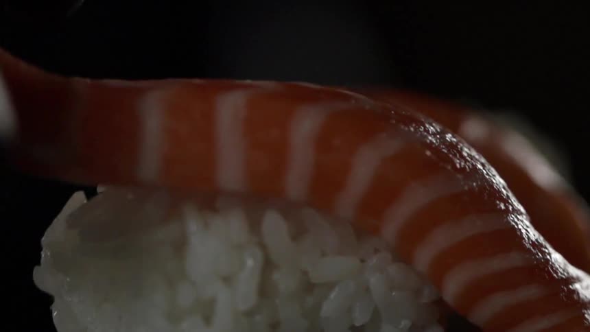 A chef places a piece of salmon on top of a ball of sushi rice