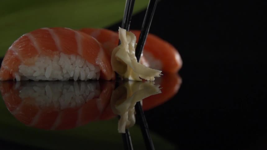 Chopsticks place ginger down next to salmon sushi