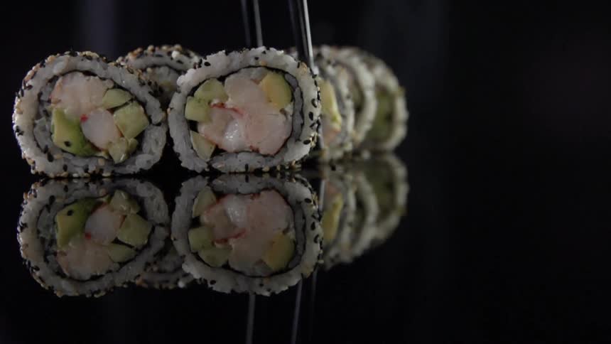 Chopsticks pick up a piece of inside out sushi roll