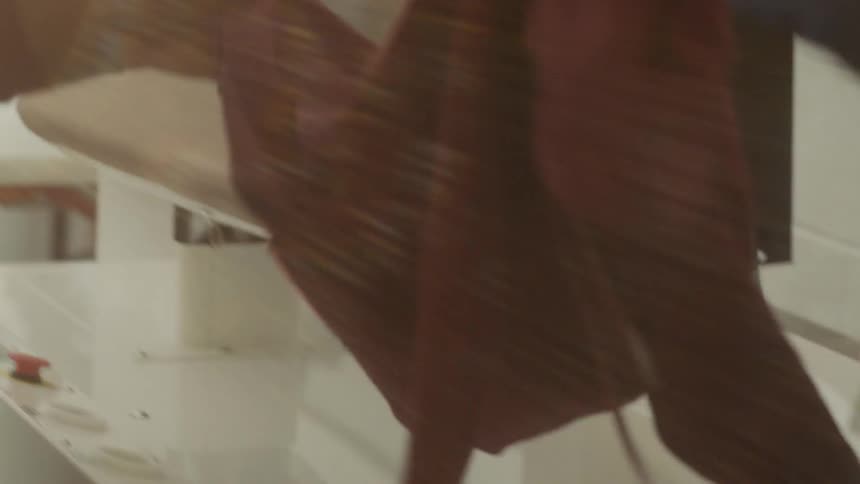 A woman lifts a garment off the pressing machine
