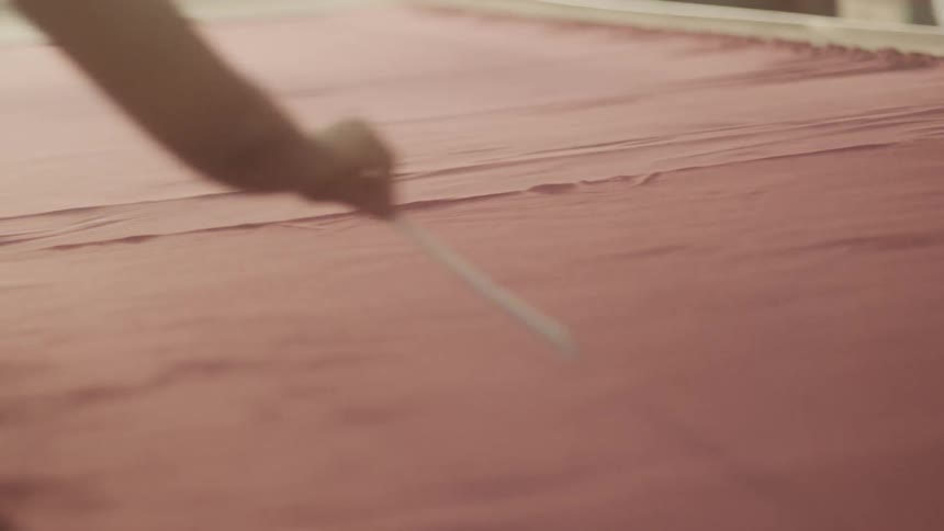 A person uses a tool to smooth the red threads on a loom
