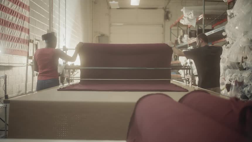 Two people roll out a large bolt of fabric