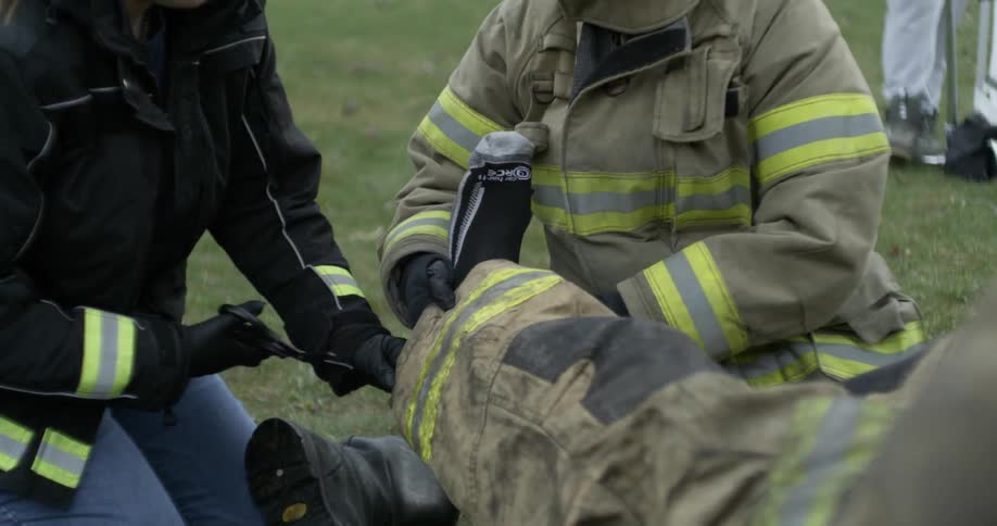 A paramedic cuts clothes from an injured firefighter
