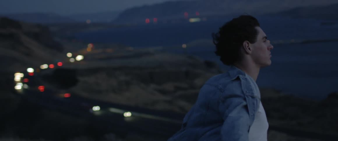 Man stands outside overlooking a highway at night