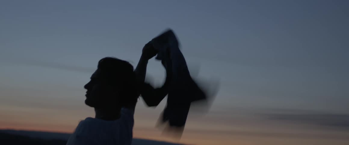 A man waves a jacket in the air in a rural field at dusk