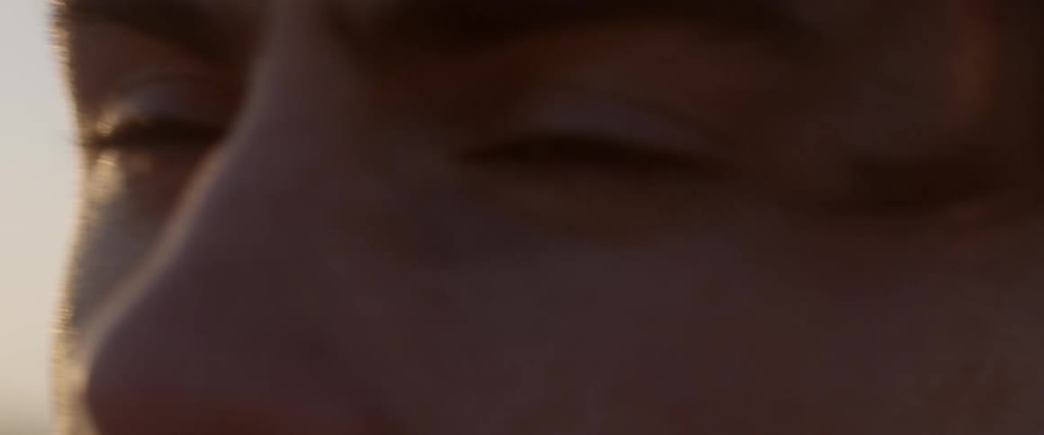 The wind is blowing the hair of a man standing outside in daylight